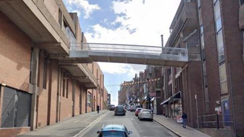 A view down North Road showing the footbridge spanning across buildings either side of the street, several meters above ground level. 