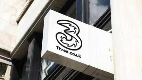 A white shop sign with the Three logo on it.