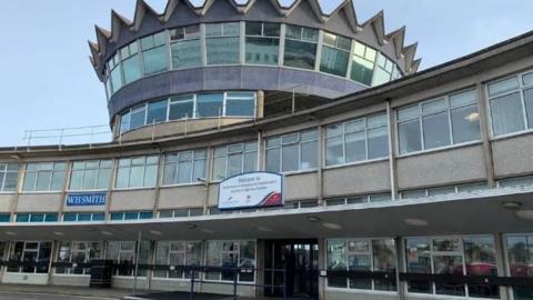 The Sea Terminal building in Douglas, which is a two-storey brown pebbledash building with large windows. It has a large turret-shaped third story in the middle that has roof with points around the edges.