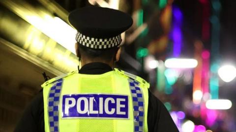 Generic image of the back of a police officer walking down a street at night