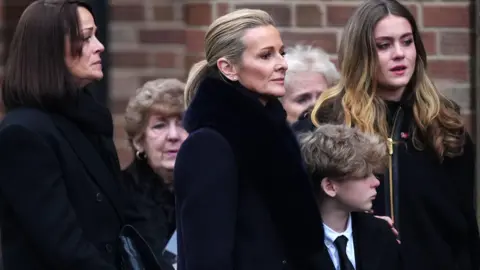 Gabby Logan and Kenny Logan with daughter Lois Maya Logan (centre right) following the funeral service for Terry Yorath at the Immaculate Heart of Mary Catholic Church in Leeds