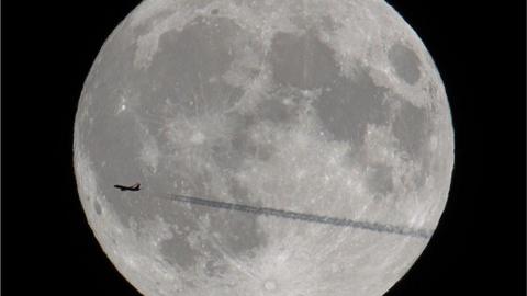 The silhouette of a plane crossing the moon.