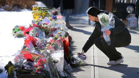 A young woman lays flowers at a memorial to victims at Brown University