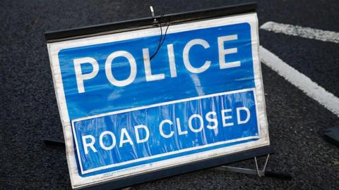 A blue sign which reads POLICE ROAD CLOSED in white letters