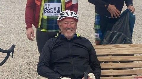 A man in a cycling helmet sitting on a bench