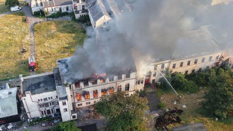 Drone shot of a burning building being hosed by firefighters. 