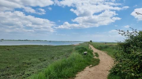 Thorney Island, a peninsula that juts into Chichester Harbour in West Sussex. The sea can be seen to the left of a walking path and grass.