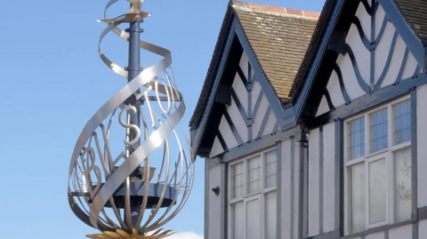 A swirling, silver sculpture spells out the name Bilston next to some black and white houses.