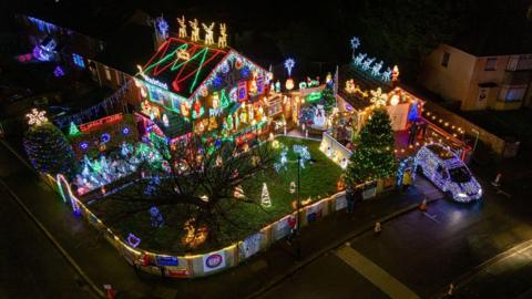 An aerial view of a house covered in Christmas lights in Brentry in Bristol. There are multiple illuminated figures in the garden including reindeer, and the roof of the house also has reindeer on it