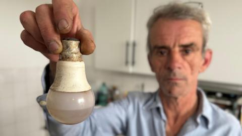 Barry holding a light bulb which has filled with water due to leaks in the extractor fan.