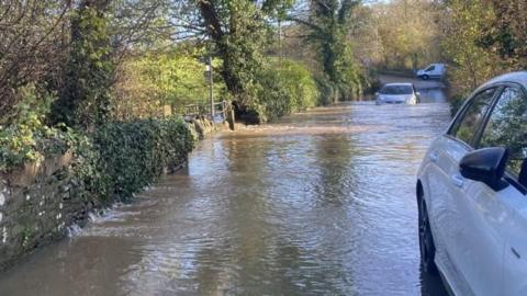 Cars stuck in flood water on a narrow lane. 