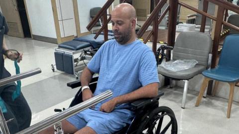 A man in a wheelchair wearing blue hospital garb.