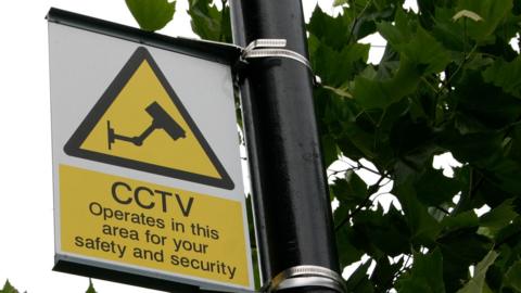 A yellow sign on a lamp-post reads: "CCTV operates in this area for your safety and security"