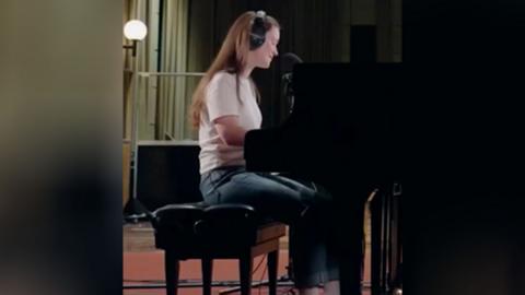 Woman with long straight hair and a white T-shirt sits at a piano