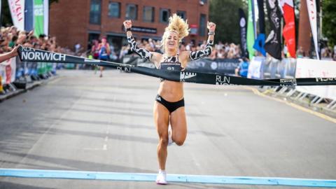 Holly Archer crossing the finish line with spectators in the background