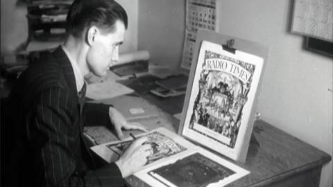 Black and white. An art editor replicating the front cover on a lineblock for printing.  The cover illustration sits on a stand in front of him, on his desk.