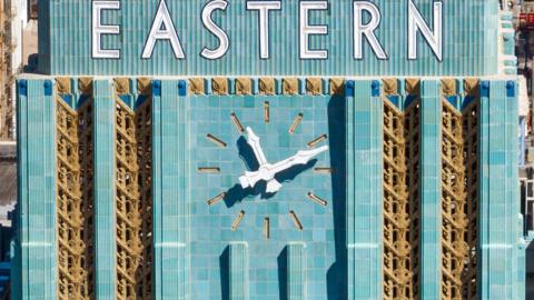 Close-up of a large blue outdoor clock underneath a sign that reads 'Eastern'