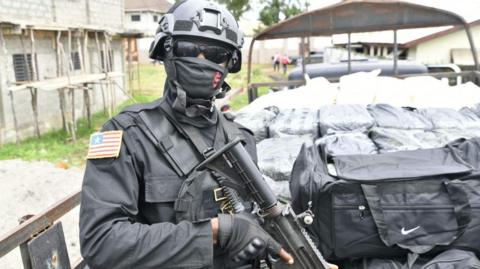 An armed Liberian police officer stands guard beside a truck carrying bags and packages 