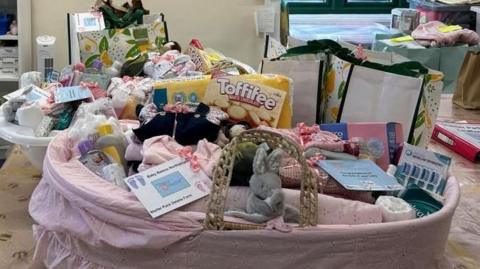 Basket covered in pink sheet contain clothing, toys and treats