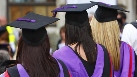 A photo from behind of three female university students wearing graduation caps and gowns.