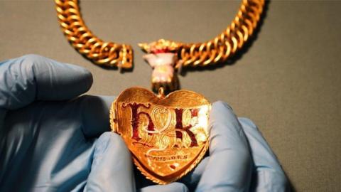 The back of a gold pendant with the letters H and K in red