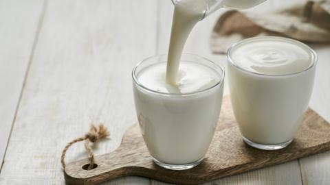 Pouring homemade kefir, from glass bottle on white wooden background. - stock photo
