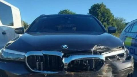 A black unmarked BMW police car that has damage to the front.