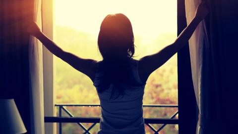 Silhouette of a person opening a pair of curtains