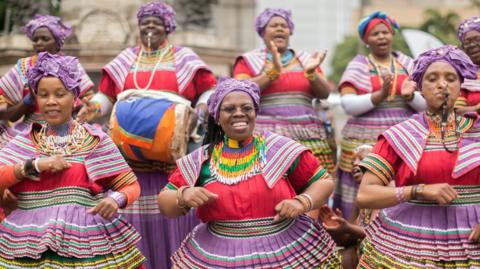 Women in traditional, multi-coloured Basotho outfits sing and dance 