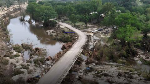 An area of trees is completely full of flood water and mud, with a road running through the centre. 