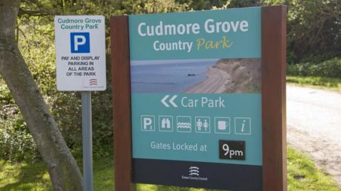 Entry sign for Cudmore Grove Country park. It advertises facilities such as parking, toilets and a cafe.