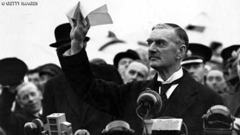 Neville Chamberlain waves a piece of paper in the air.