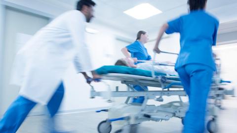 A doctor and two nurses rush through a hospital corridor with a patient on a trolley. 