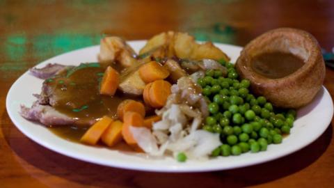 A plate of Sunday roast dinner, with meat covered in gravy, potatoes, carrots, peas and a Yorkshire pudding.