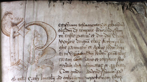A paragraph of Latin text within a probate register, including a large letter R illustrated by two entwined dragons. The writing is clearly old, and the paper is worn and burned at the edges.
