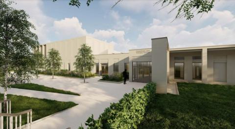 An artist's impression of the new school, with its name above the front door. The building is stone coloured with black framed windows and there's greenery outside.