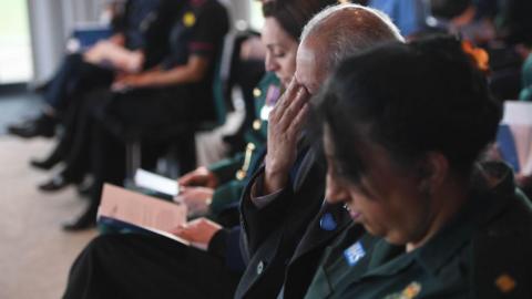 A number of people in green NHS uniforms sat in a row with their heads bowed