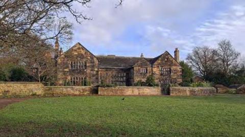 A large historic stone manor house set within an open, grassy landscape.