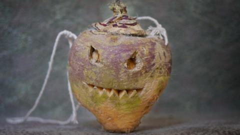 A turnip carved with a spooky face carved in the style of a pumpkin, with string attached for carrying. 