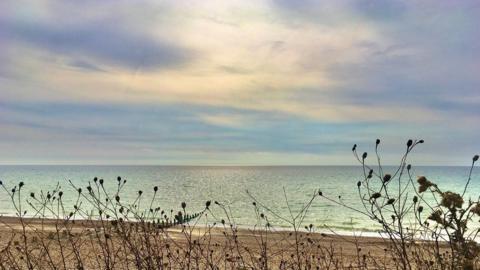 Weak yellow sun lights up high clouds with blue sky and greeny blue sea below