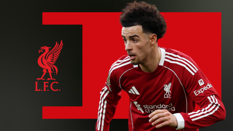 Curtis Jones in Liverpool home kit during a match, in front of a red and black background and the club badge