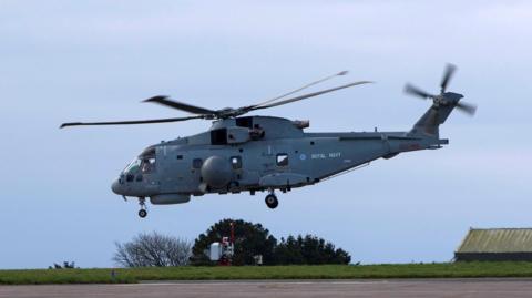 The Royal Navy Merlin Mk2 helicopter taking off from RNAS Culdrose on Saturday. It is on a concrete runway on a clear day. 