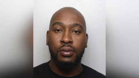 Blessing Mudzinge custody image. He is bald and has a dark beard. He wears a black T-shirt.