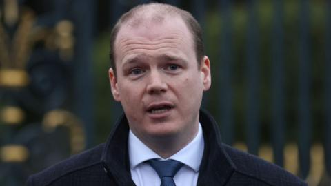 Gordan Lyons wearing a white shirt, black tie and black coat 