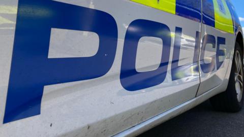 A close-up of a police car, with the word 'police' written in large blue letters on the white body of the car.