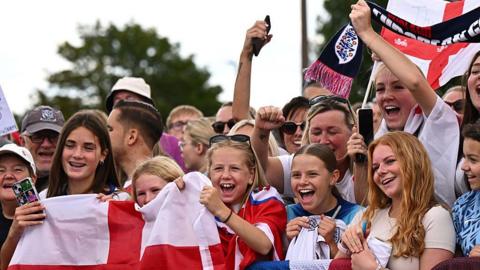 Fans holding flags and posters wait at Southend Airport to see England's Women return 