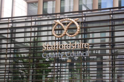 The front of a Staffordshire County Council building. It has the sign "Staffordshire County Council" on the front of the building which has glass with metal frames.