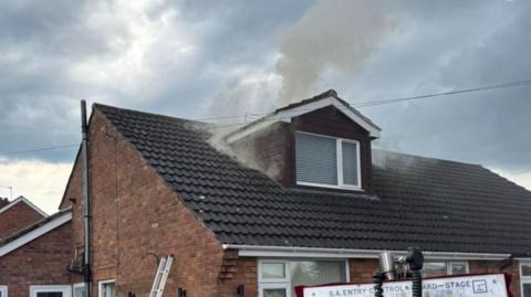 A small amount of smoke rising from a dormer window in the roof of a semi-detached house.