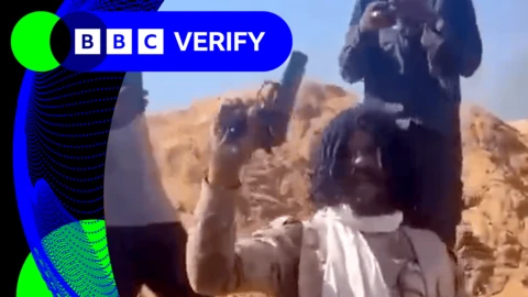 A man in camouflage holding a pistol in the air