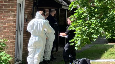 Forensic officers and police officers stood outside of a brick property.
